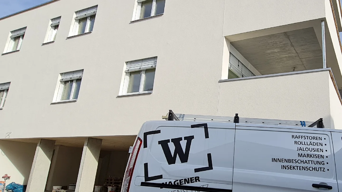 Firmenfahrzeug von Wagener Sonnenschutz mit dem Zeichen W im Eckrahmen und der Leistungsliste auf der Seite, dahinter ein Wohnhaus mit Raffstoren