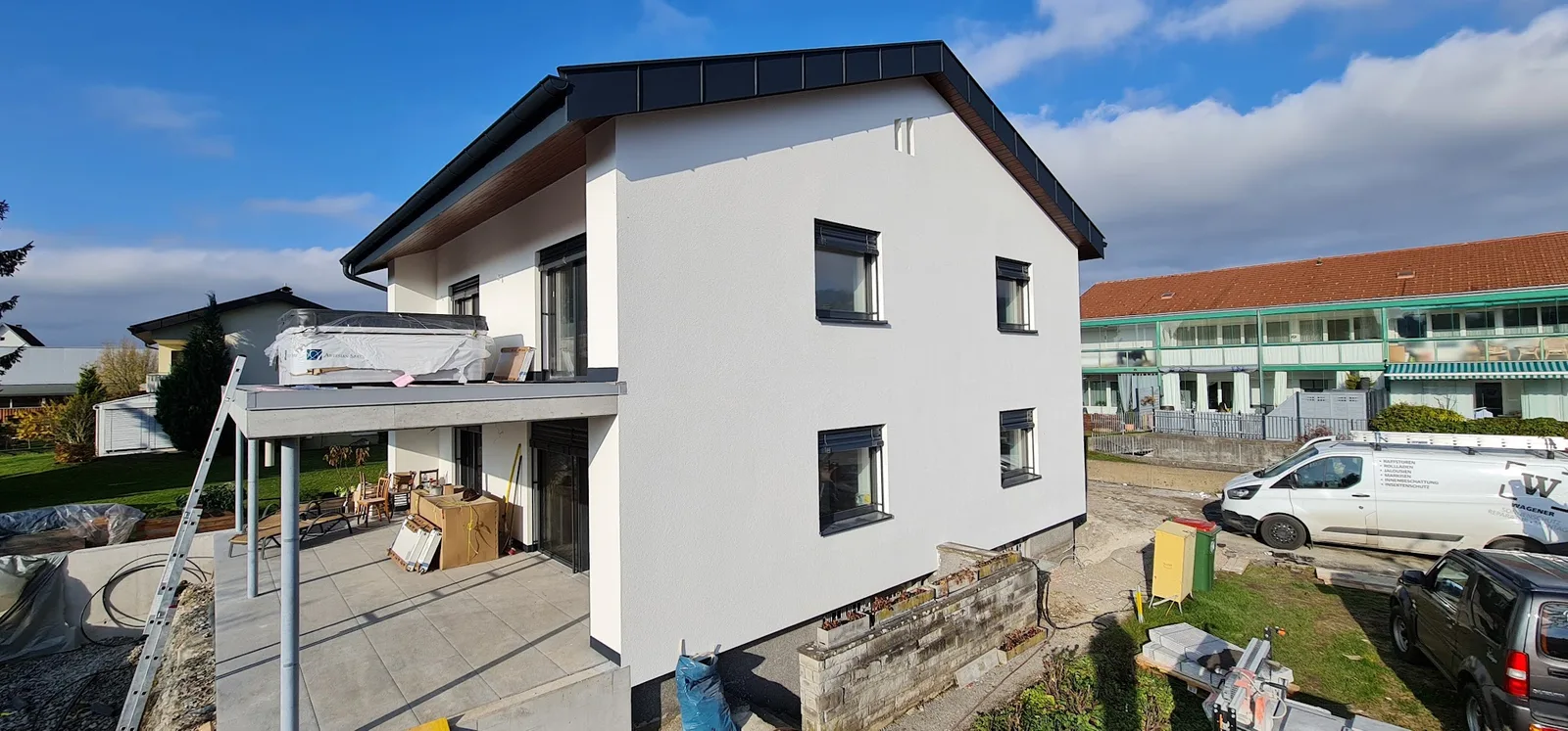 Neu gebautes Wohnhaus mit dunklen Raffstoren an allen Fenstern, rechts das Firmenfahrzeug von Wagener Sonnenschutz