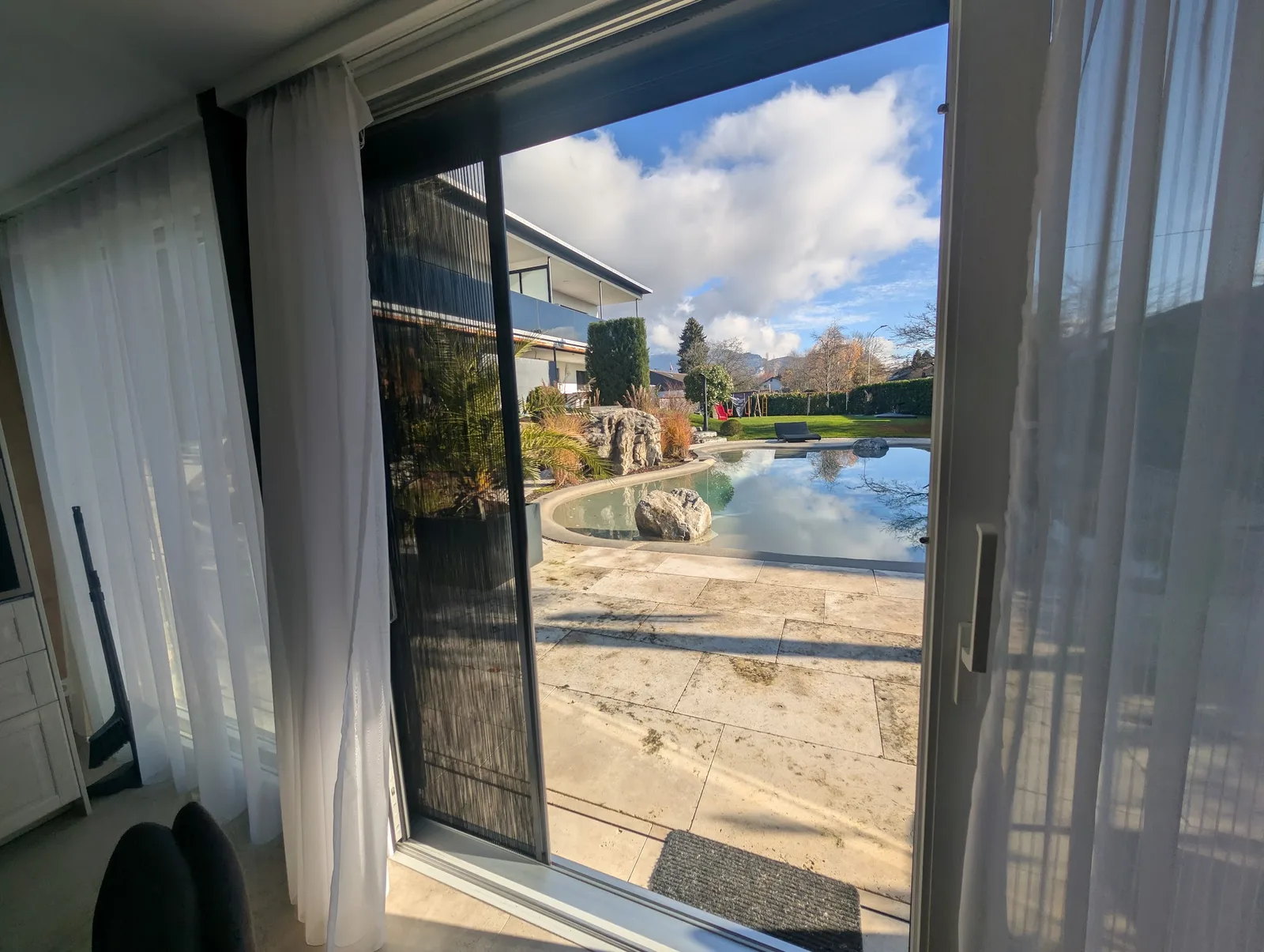 Insektenschutz-Plissee in einer geöffneten Schiebetür, Blick auf Pool und Garten