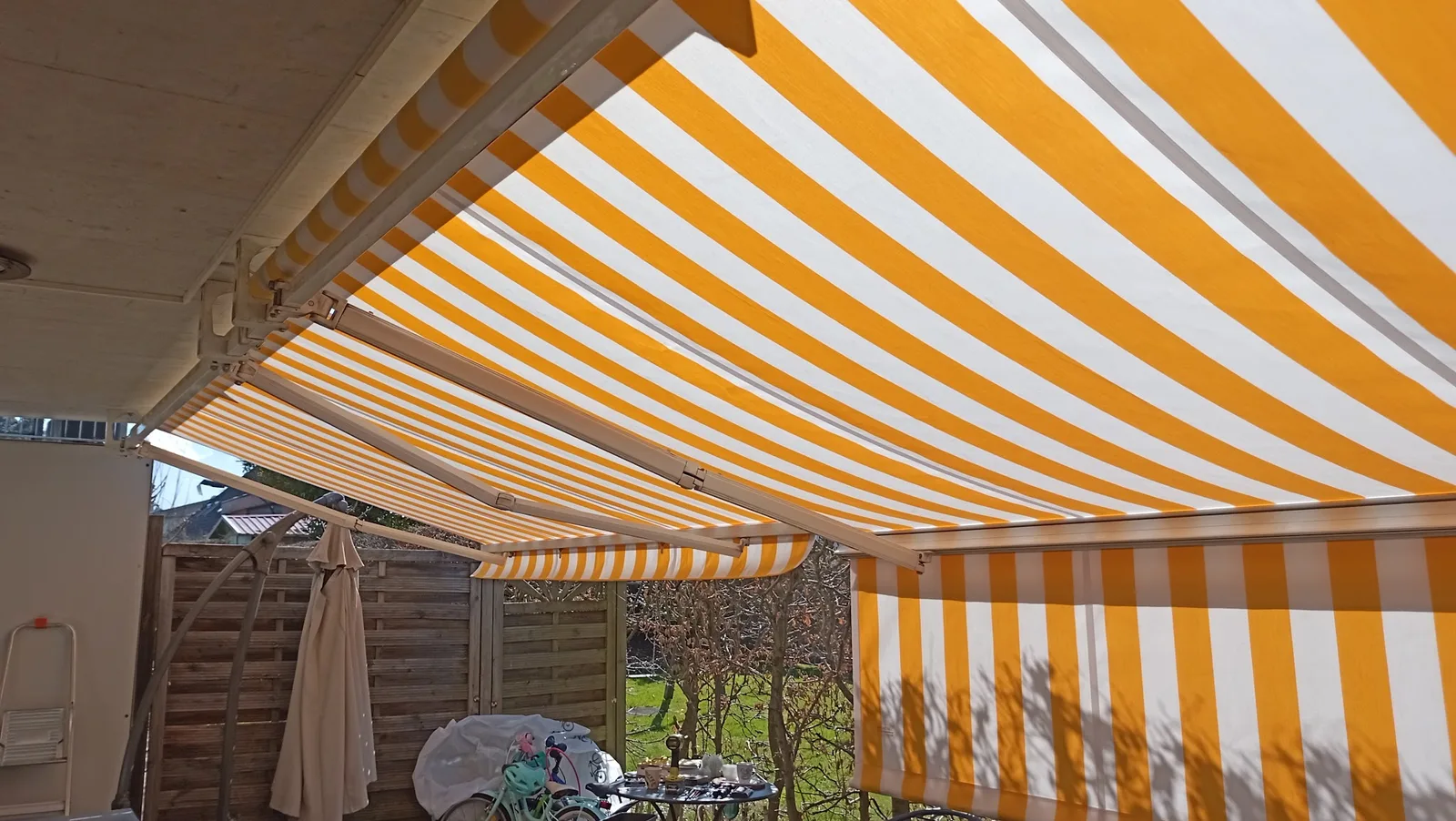 Gelb-weiß gestreifte Gelenkarmmarkise mit ausgefahrenem Volant über einer Terrasse